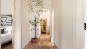 Un pasillo estrecho con suelo de madera, una planta en maceta y una cama a la izquierda.
