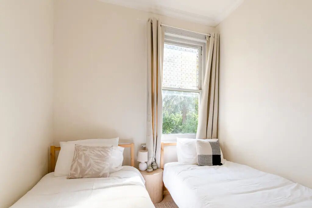 Una habitación pequeña y luminosa con dos camas, una ventana con cortinas y vistas a zonas verdes.