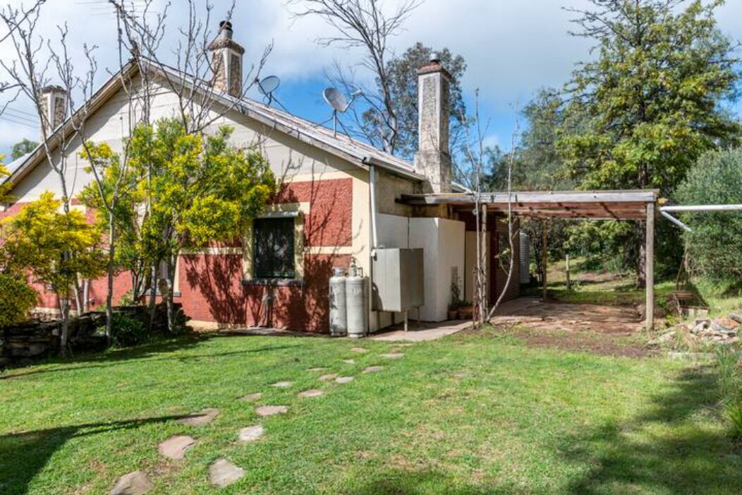 A house with a covered patio, a chimney, and a yard with a lawn and trees.