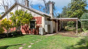 A house with a covered patio, a chimney, and a yard with a lawn and trees.