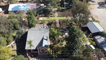 An aerial view of a residential property with a large house featuring a metal roof, a small attached garage, and a well-maintained garden with a variety of plants and a stone pathway.