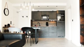 Une cuisine moderne avec des meubles de couleur sombre, un four à micro-ondes et un four encastré. On y trouve également un coin repas avec un canapé en cuir noir et une table ronde en bois.