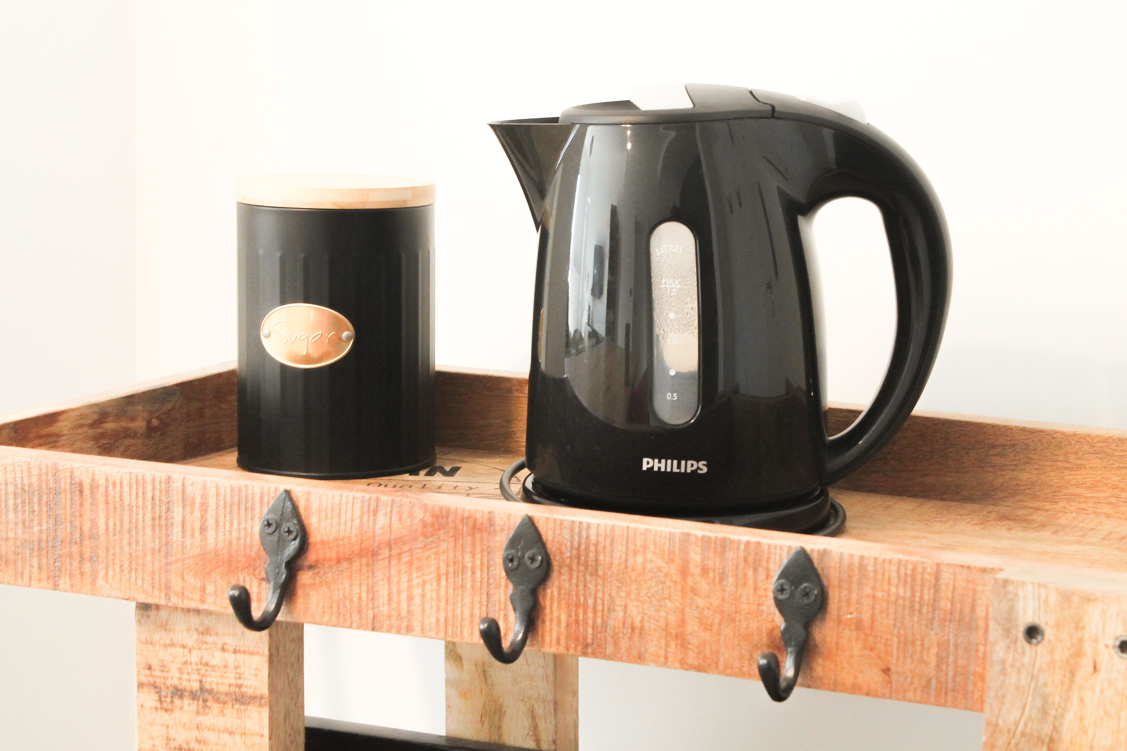 A black coffee maker and mug on a wooden tray with metal hooks.