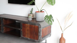 Une console en bois sur laquelle est fixée une télévision, agrémentée de deux plantes en pot et d’un vase contenant des herbes des pampas séchées.