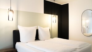 Un lit bien fait, avec du linge de lit blanc, une table de chevet en bois et deux appliques murales.