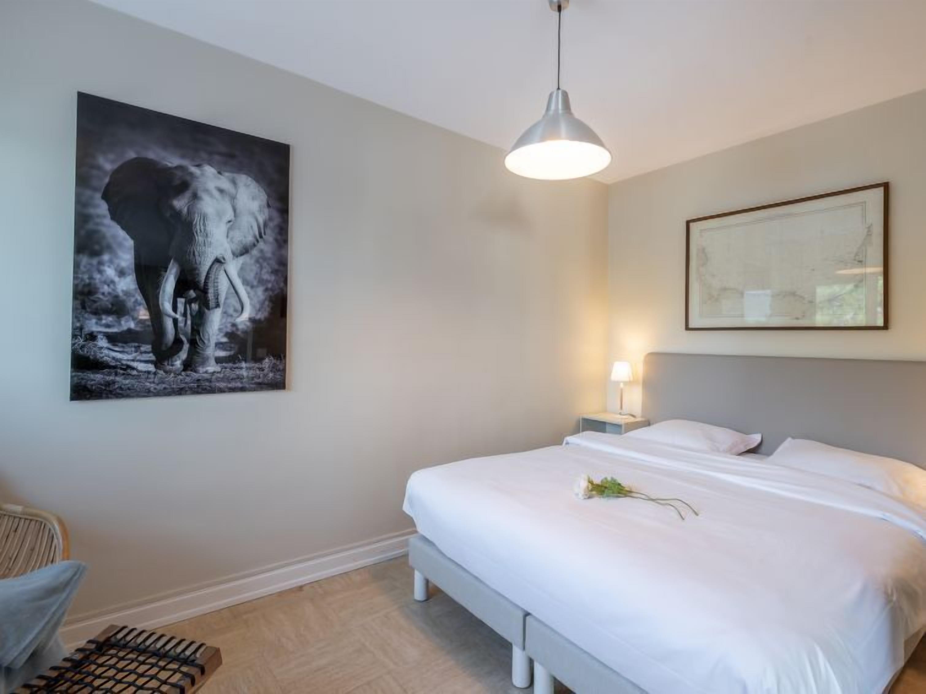 A bedroom with a bed, a nightstand, a lamp, a chair, and artwork on the walls.