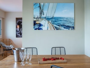 Ein Essbereich mit Holztisch, einem Metallkübel und Weingläsern. An der Wand hängt ein Segelboot-Bild, und es gibt zwei Stühle.