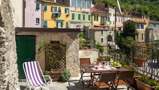 Eine Terrasse mit einem Essplatz, umgeben von Steinmauern und farbenfrohen Gebäuden im Hintergrund.