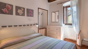 Ein Schlafzimmer mit Bett, Kommode, Spiegel und einem Fenster mit Vorhängen.