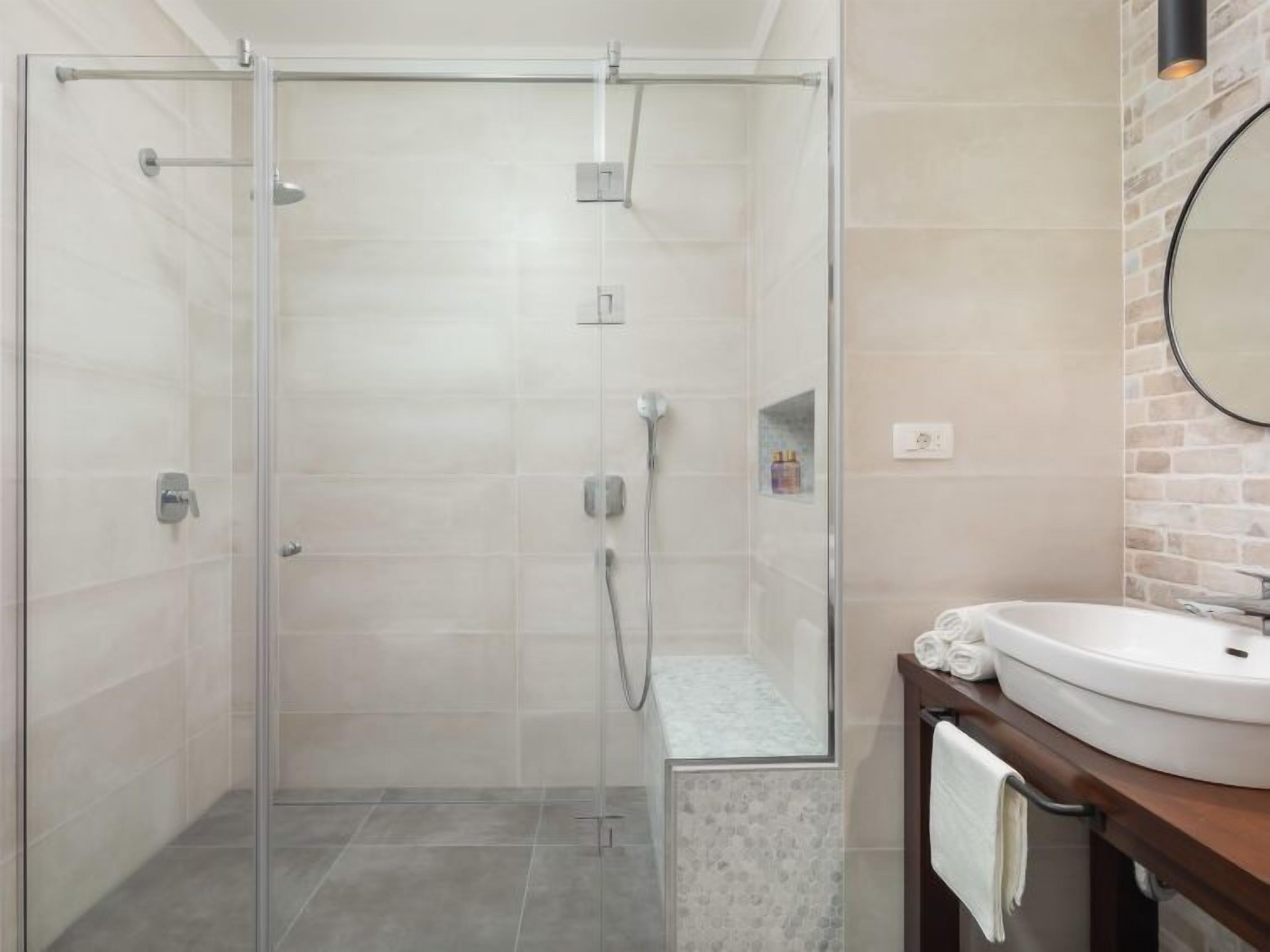 Un baño moderno con ducha de vidrio, lavamanos blanco y espejo con marco redondo.