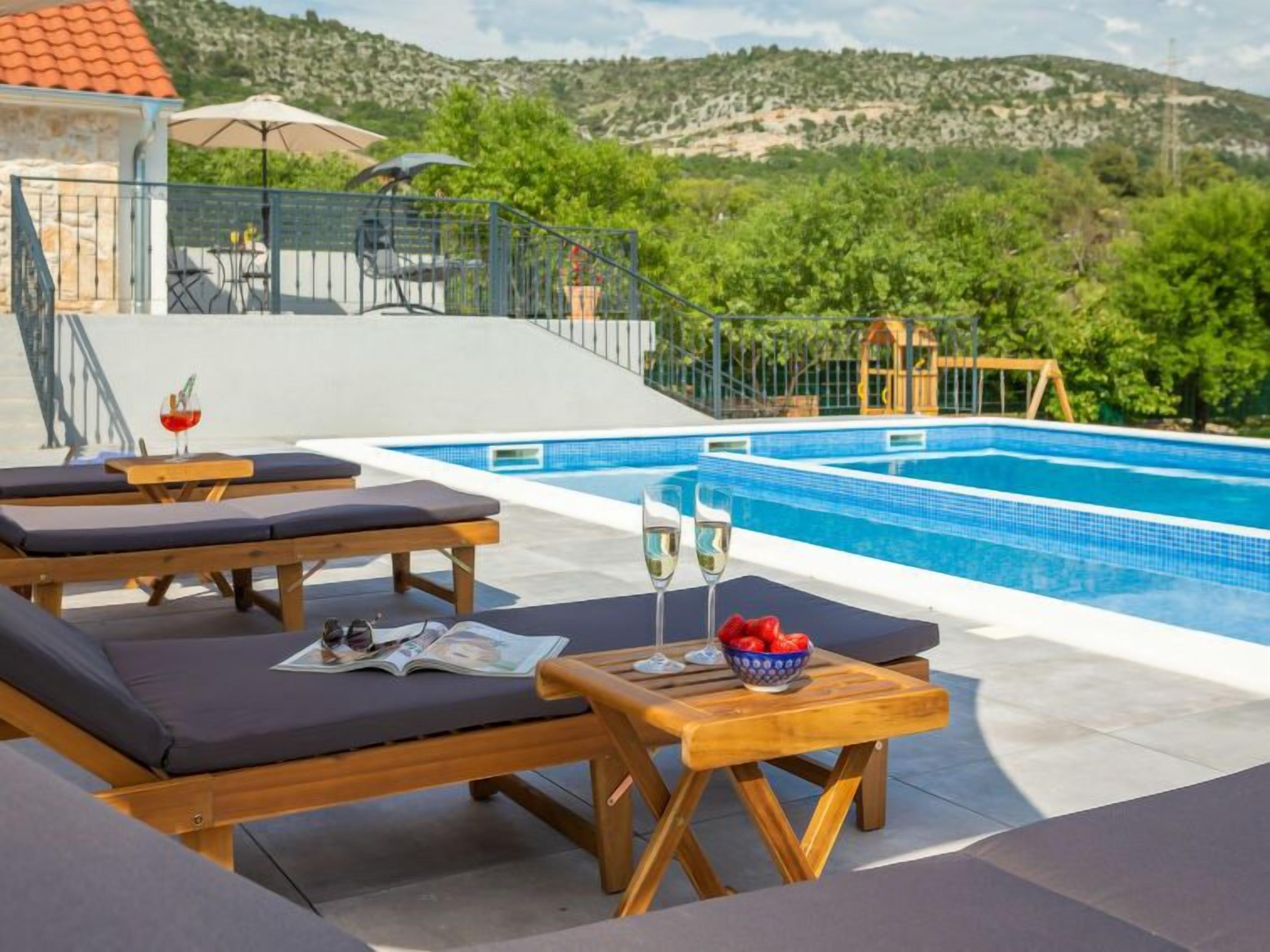 Un espace aménagé au bord de la piscine, avec des chaises longues et une table, un verre de vin et un saladier de fruits.