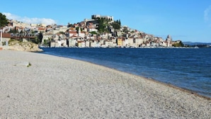 A coastal town with a historic hilltop castle, a pebble beach, and a clear blue sky.