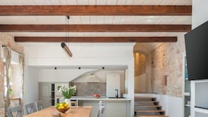 A spacious kitchen with a wooden table, chairs, and a fruit bowl. There is a staircase leading to an upper level.