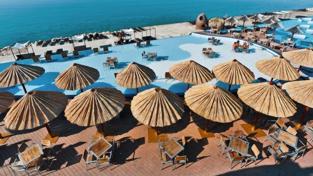 A resort pool area with sun umbrellas, lounge chairs, and a view of the sea.
