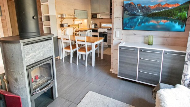 Ein modernes Blockhaus-Interieur mit Kamin aus Stein, Holztisch und großem Flachbildfernseher an der Wand.