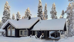 Ein schneebedecktes Holzhaus mit großer Veranda und Schornstein.