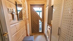Ein schmales Entree mit Holzwänden, einer Tür mit Rautenmuster, einer Waschmaschine und einem Schrank mit gelochter Front.