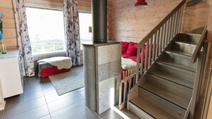 Ein Holzblockhaus-Interieur mit Kamin aus Stein, einem roten Sofa und einer Treppe.