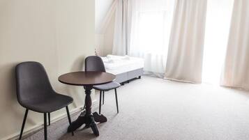 Una habitación de hotel con cama, dos sillas, una mesita redonda y un ventanal con cortinas.