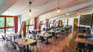 A spacious dining area with multiple tables and chairs, large windows with curtains, and hanging light fixtures. - Perła Świeradowa (Swieradow-Zdroj)