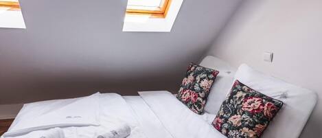 Un dormitorio con cama, dos almohadas, una ventana y una toalla en el suelo.
