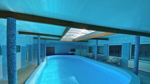 An indoor swimming pool with a tiled floor, a glass ceiling, and seating areas along the sides. - Perła Świeradowa (Swieradow-Zdroj)