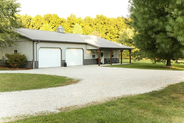A two-story metal building with a garage, covered porch, and a gravel driveway. - Quiet Indiana Getaway w/ Game Room (Moores Hill)