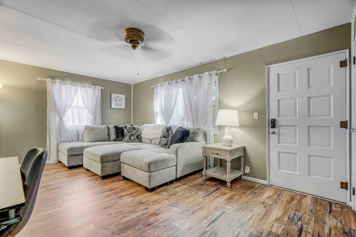 Una habitación con sofá modular, una mesita con lámpara, una puerta y un ventilador de techo.