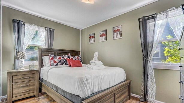 Ein Schlafzimmer mit einem hölzernen Bett, einem Nachttisch, einem Fenster mit Vorhängen und Wandbildern.