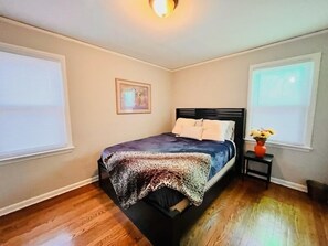 Ein Schlafzimmer mit einem Bett, einem Nachttisch, einem gerahmten Bild und einem Fenster mit Jalousien.