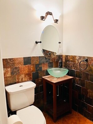 Ein Badezimmer mit weißer Toilette, einem Waschbecken aus Glas und einer gefliesten Rückwand.