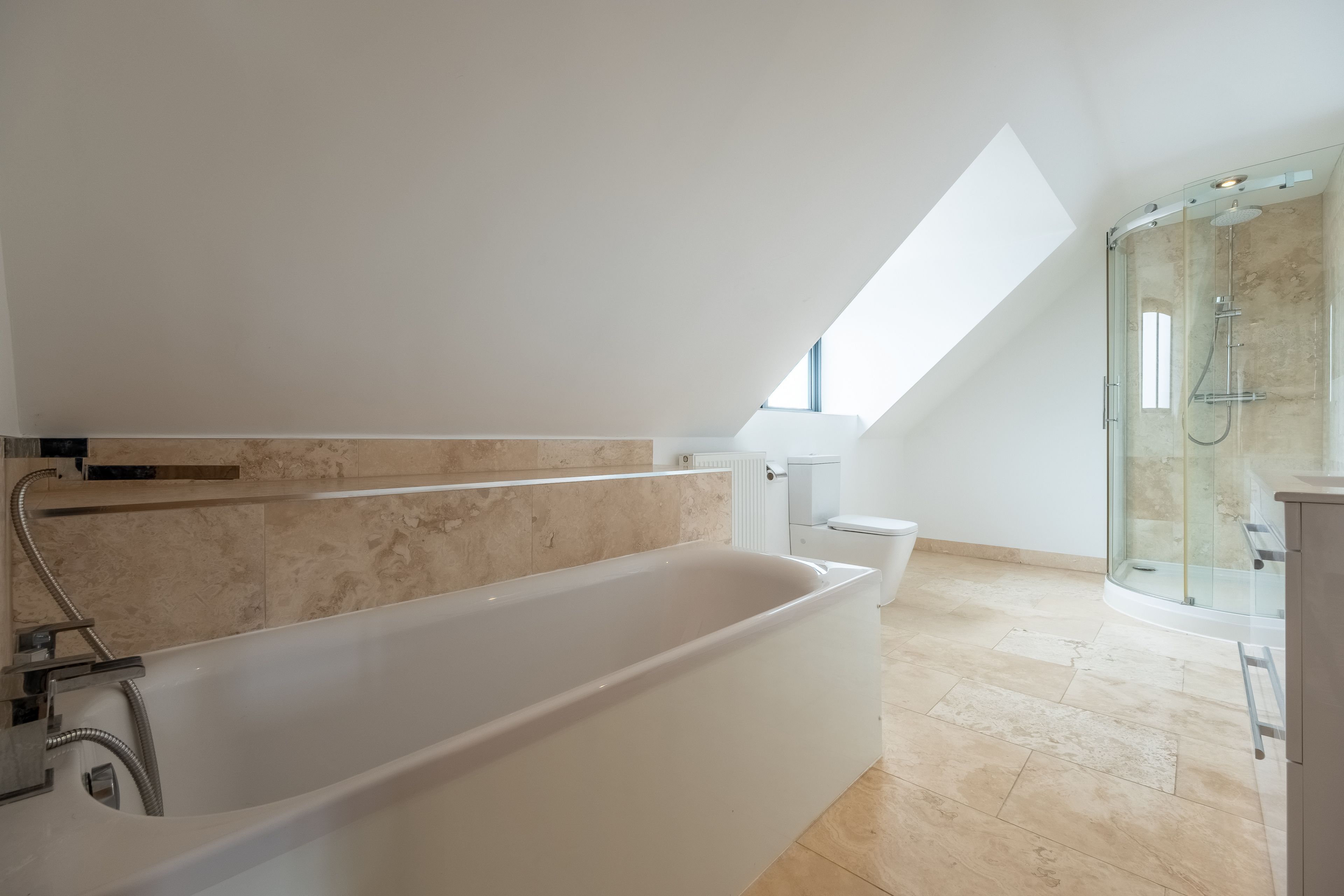 Een moderne badkamer met een vrijstaand bad, een douche met glazen wanden en een dakraam.