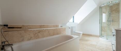 Een moderne badkamer met een vrijstaand bad, een douche met glazen wanden en een dakraam.