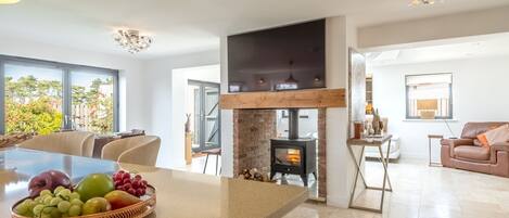 A modern kitchen with a central island, a built-in wood stove, and a dining area with a large window.