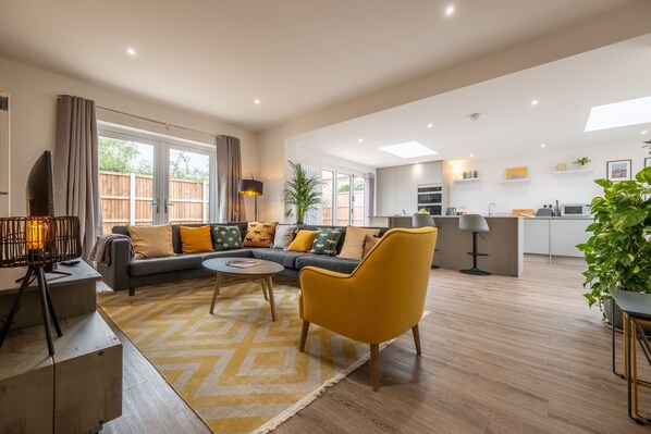 A spacious living area with a sofa, armchairs, and a coffee table. There is a kitchen in the background with modern appliances and a dining area. - Little Soames, Holt, Norfolk (Holt)