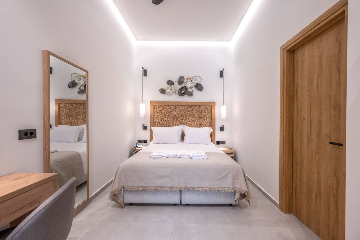 A modern hotel room with a large bed, bedside tables, a wooden wardrobe, and a mirror.