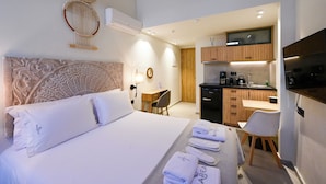 A hotel room with a bed, a desk, a chair, a kitchenette, and a TV. - Marea Boutique Suites (Rethymno)