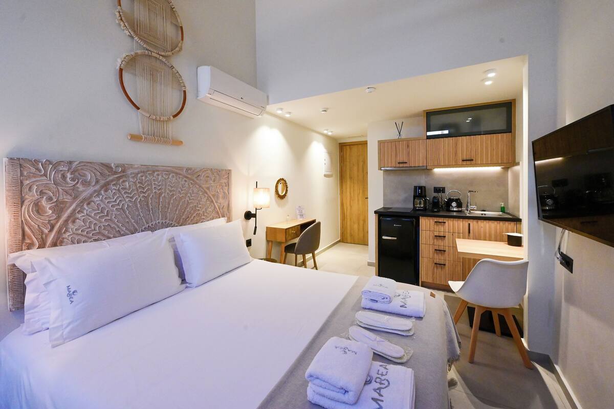 A hotel room with a bed, a desk, a chair, a kitchenette, and a TV.