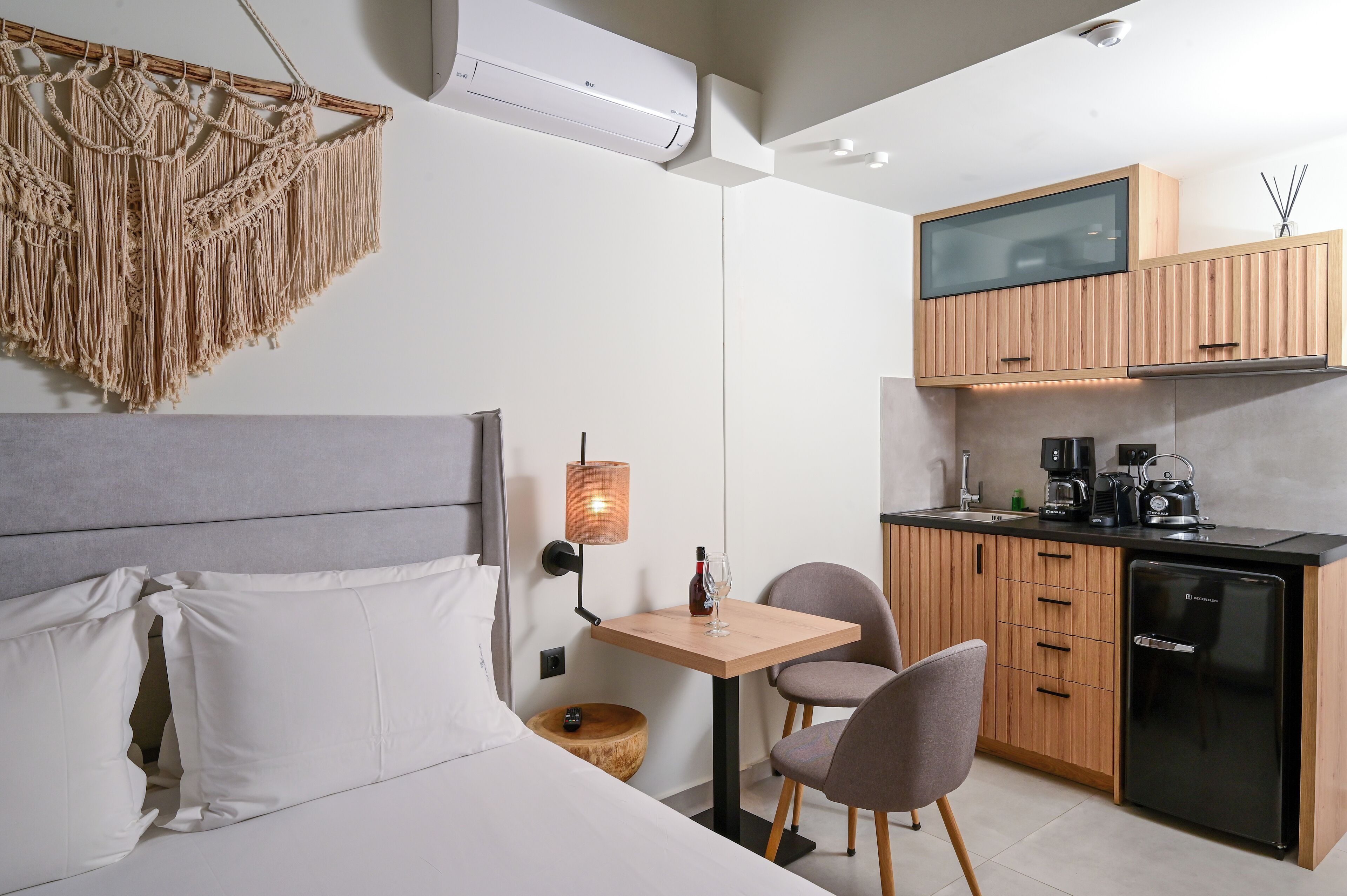A compact hotel room with a bed, a small table with chairs, a kitchenette, and a TV mounted above the counter.