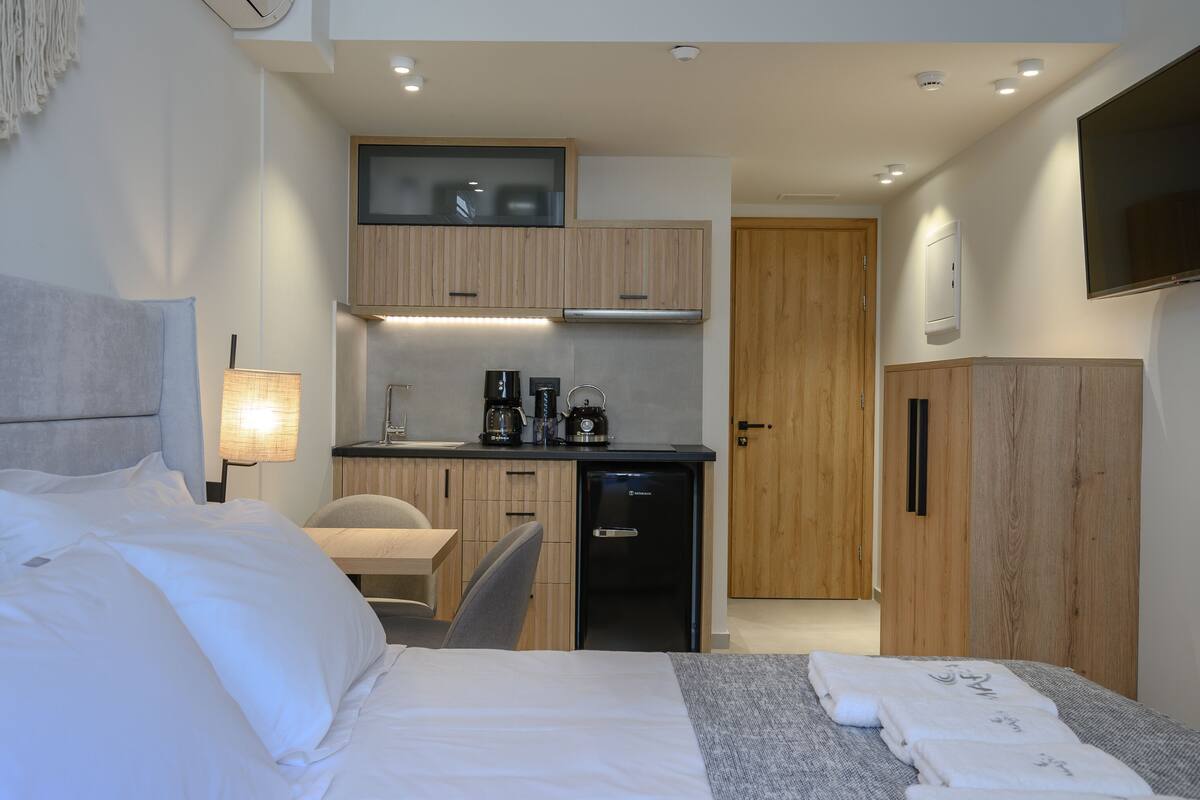 A modern hotel room with a bed, a desk with a coffee maker, a small refrigerator, and a TV mounted on the wall.