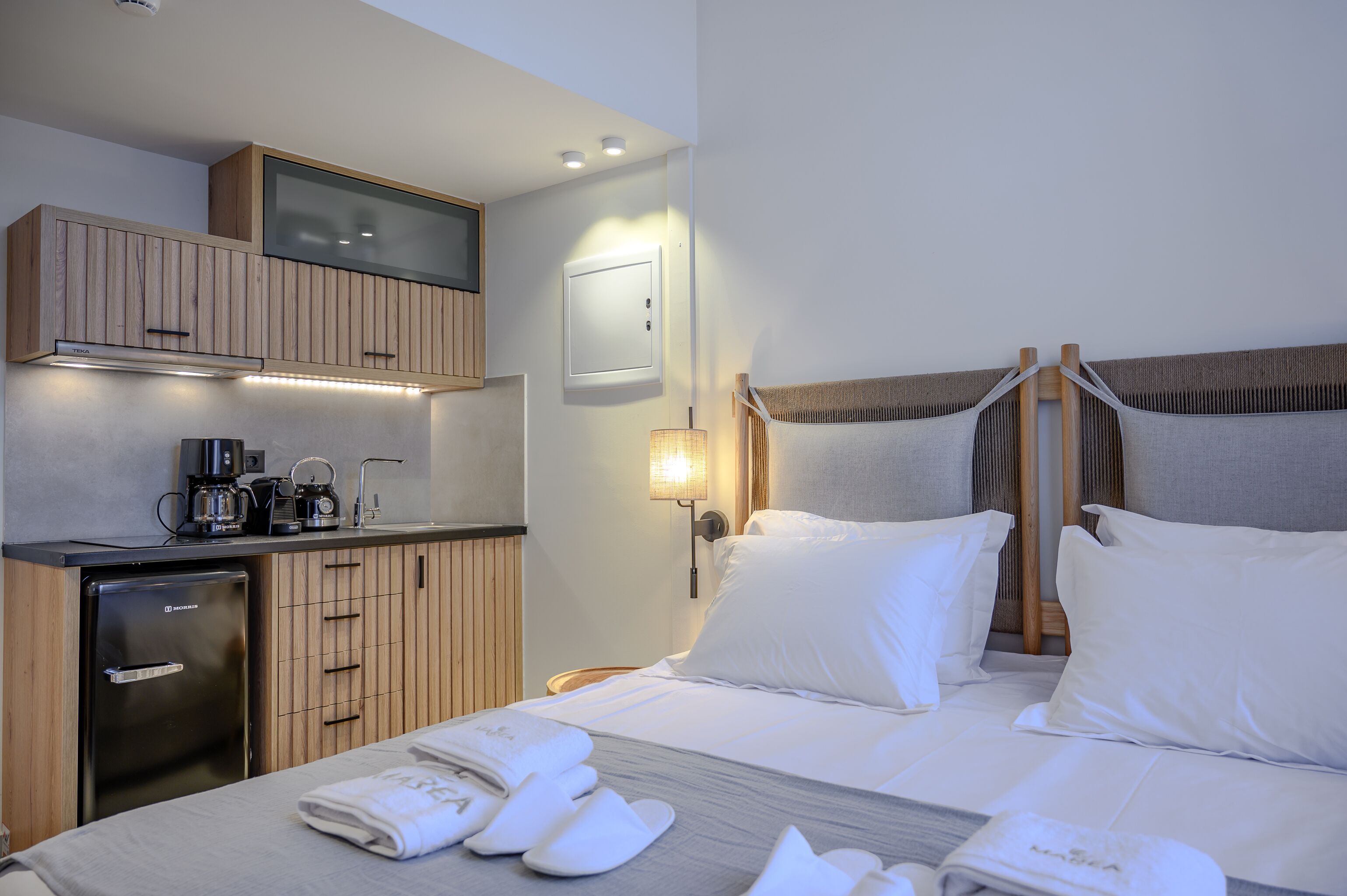 Ein Hotelzimmer mit Bett, einer kleinen Küchenzeile, einem Fernseher und einem Nachttisch.
