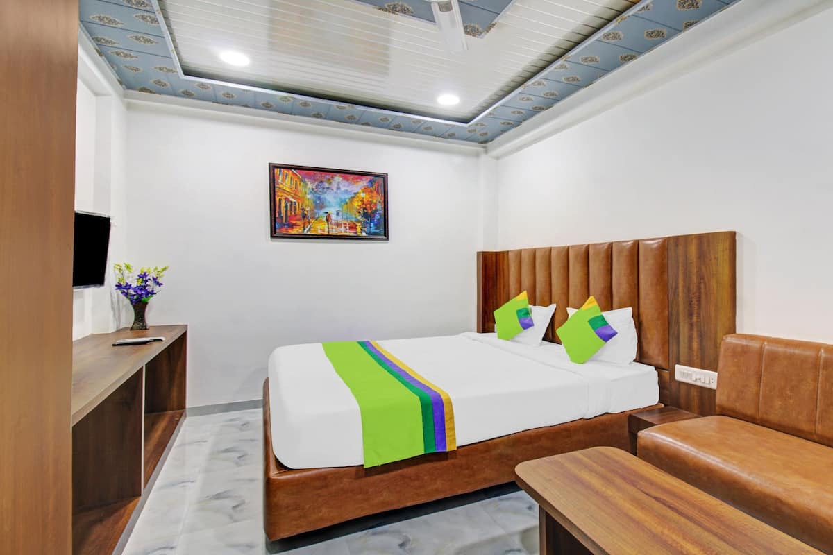 Quarto de hotel com uma cama, um banco de madeira, uma escrivaninha com um vaso de flores e um quadro na parede.