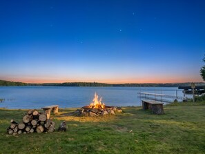 Un feu de camp au bord du lac, avec un quai et une pile de bûches.