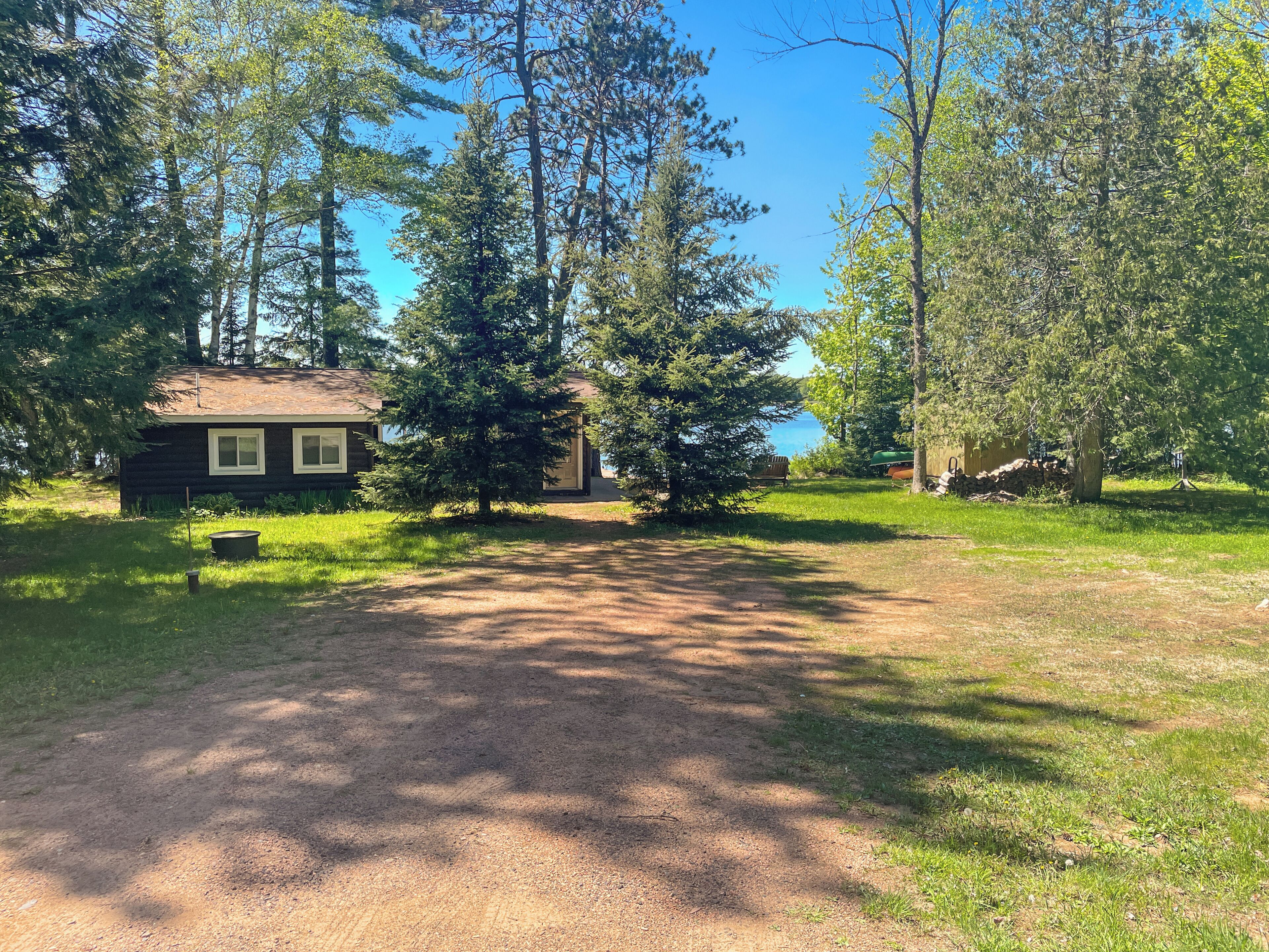 A cabin with a dirt path leading to it, surrounded by trees and a clear sky.