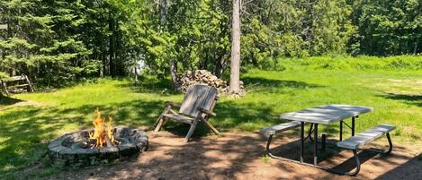 Un camping con una fogata, una silla de madera y una mesa de picnic.