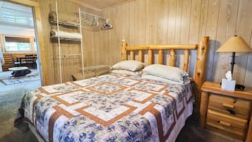 Une pièce aux murs lambrés, avec un lit, une table de chevet dotée d’une lampe et un portant à vêtements suspendu.