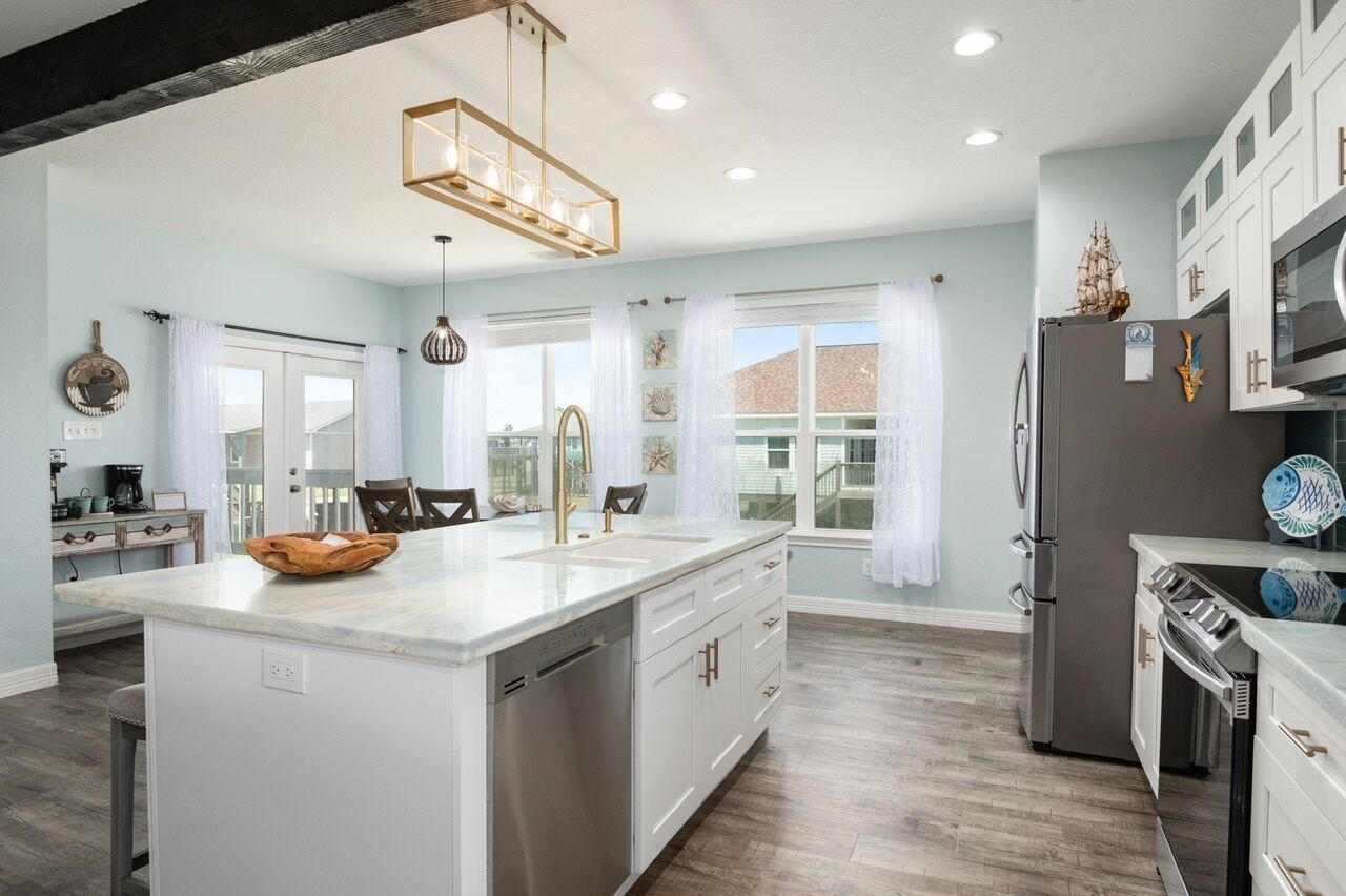 A modern kitchen with a central island, stainless steel appliances, and light blue walls.