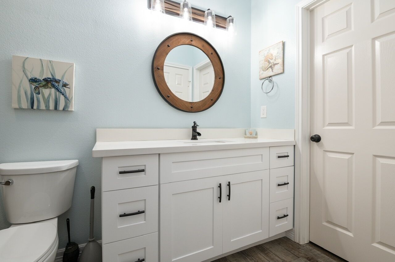 Un baño con inodoro blanco, lavamanos con espejo arriba y una puerta a la derecha.