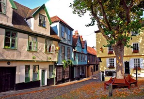 A cobblestone street lined with traditional European buildings, some with green shutters and others with white trim.