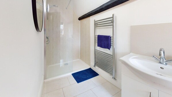 A bathroom with a glass shower enclosure, a towel rack with a towel, a sink, and a blue mat on the floor.